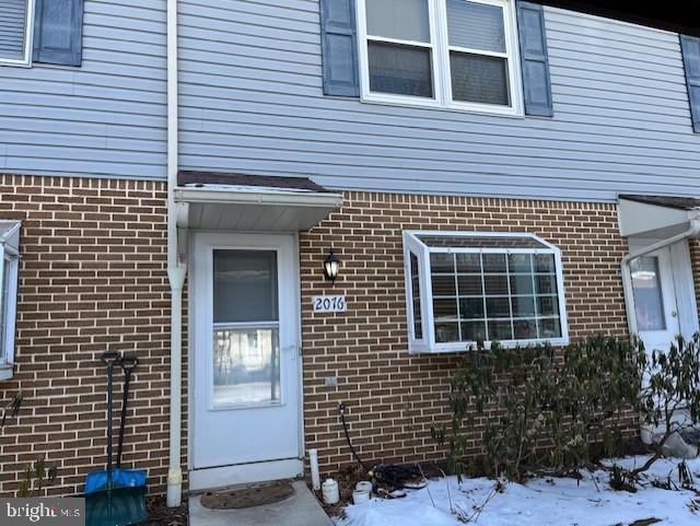 snow covered property entrance featuring brick siding