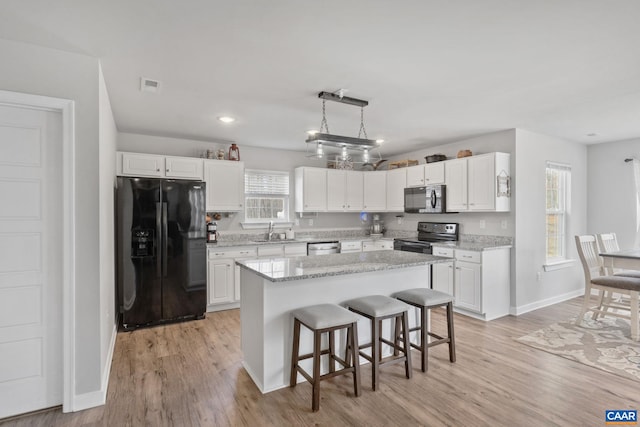 kitchen with black appliances, light wood-style flooring, a kitchen breakfast bar, white cabinetry, and a sink