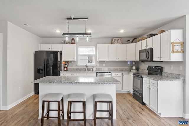 kitchen with black appliances, a sink, a kitchen breakfast bar, white cabinets, and light wood finished floors