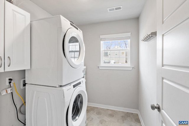 washroom with stacked washer / dryer, cabinet space, baseboards, and visible vents