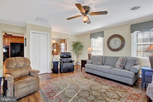 living area featuring visible vents, ornamental molding, a baseboard heating unit, wood finished floors, and ceiling fan