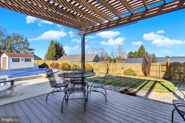 wooden terrace featuring an outbuilding, outdoor dining area, a fenced backyard, and a pergola