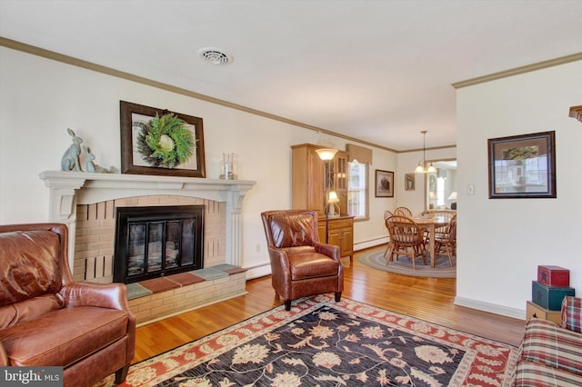 living area with baseboard heating, a brick fireplace, crown molding, and wood finished floors