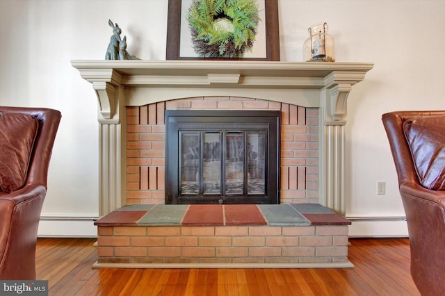 room details featuring a baseboard heating unit, wood finished floors, and a fireplace