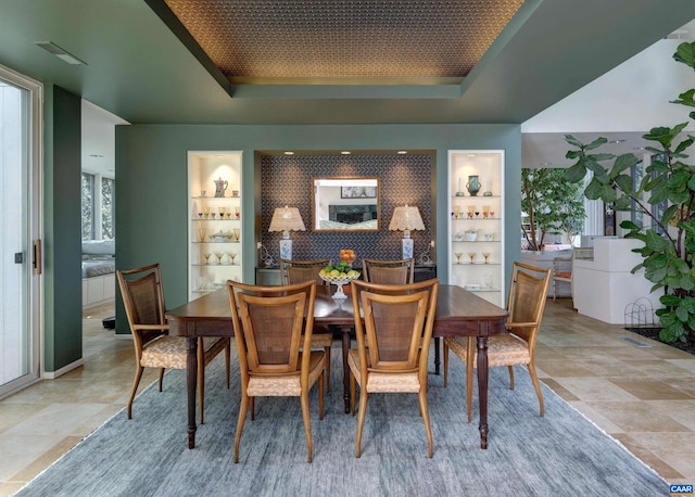 dining area with a raised ceiling and built in shelves