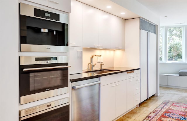 kitchen featuring dark countertops, recessed lighting, stainless steel appliances, white cabinetry, and a sink