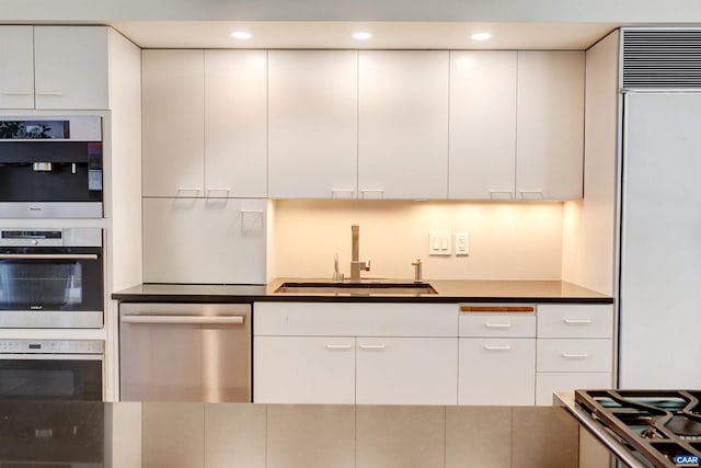 kitchen featuring white cabinetry, dark countertops, appliances with stainless steel finishes, and a sink