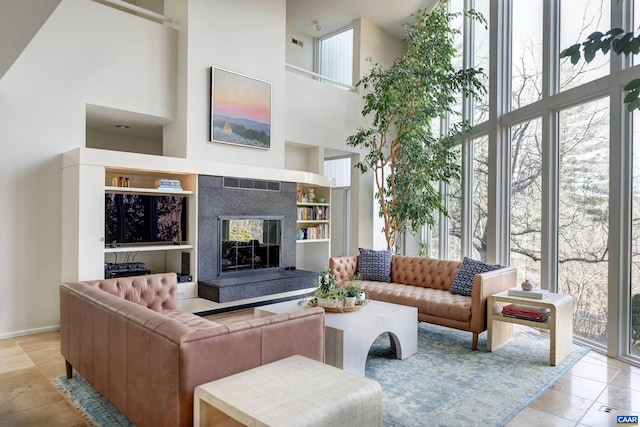 living room with a tiled fireplace, built in features, tile patterned flooring, and a high ceiling