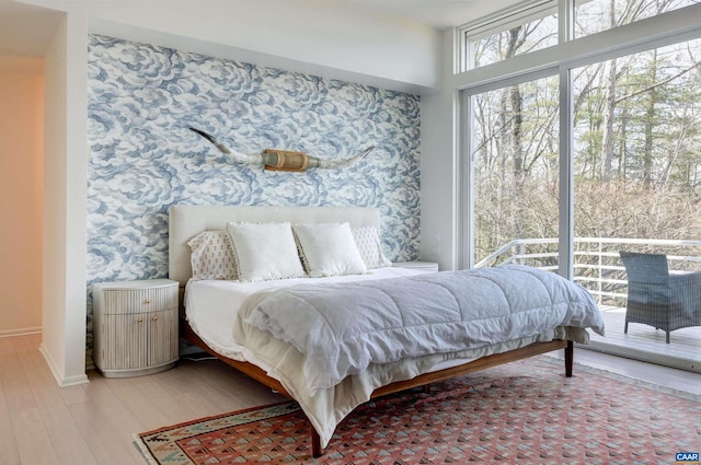 bedroom featuring wallpapered walls, access to exterior, light wood finished floors, and an accent wall