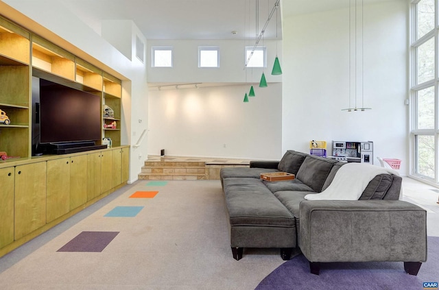 living area with visible vents, rail lighting, a towering ceiling, and built in shelves