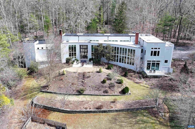 rear view of house featuring stucco siding, entry steps, a chimney, and a view of trees