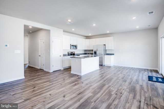 kitchen with a center island with sink, stainless steel appliances, open floor plan, and light wood-style flooring