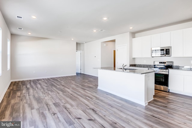 kitchen with stone countertops, stainless steel appliances, an island with sink, and recessed lighting