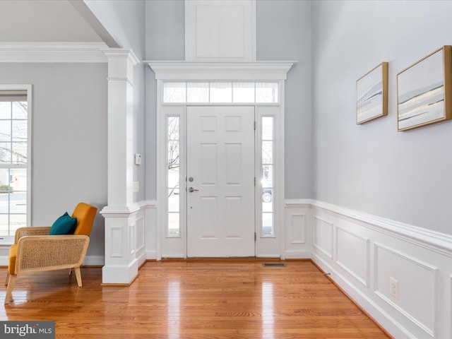 entryway featuring a wealth of natural light, ornamental molding, light wood-type flooring, and decorative columns