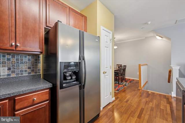 kitchen featuring stainless steel refrigerator with ice dispenser, crown molding, dark countertops, tasteful backsplash, and wood finished floors