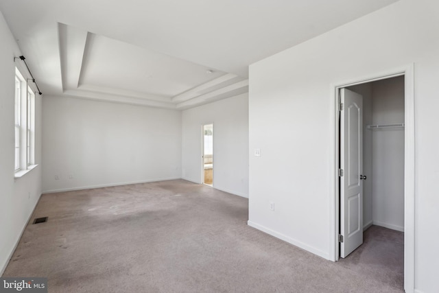 interior space featuring carpet, visible vents, baseboards, a tray ceiling, and a spacious closet