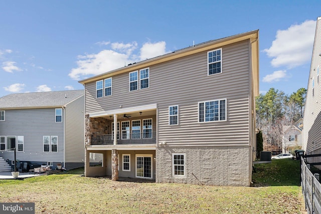 back of property with a balcony, a ceiling fan, central AC unit, fence, and a yard