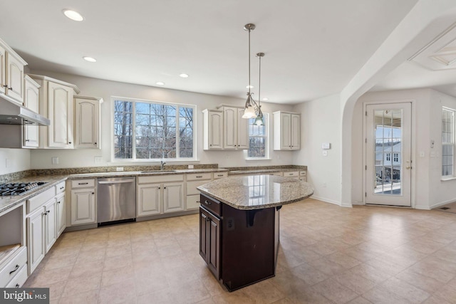 kitchen with light stone countertops, arched walkways, a sink, under cabinet range hood, and appliances with stainless steel finishes