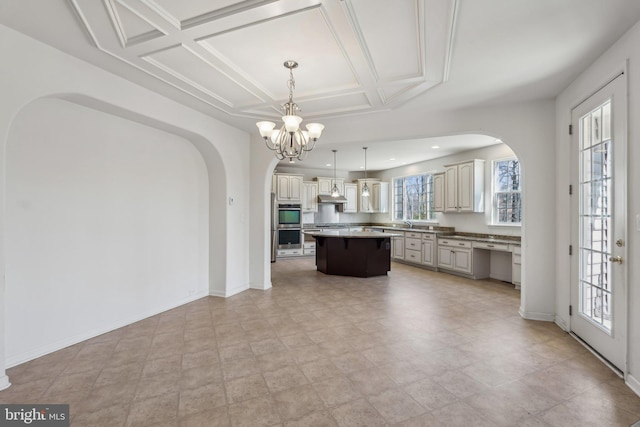 kitchen featuring under cabinet range hood, coffered ceiling, a center island, baseboards, and a chandelier