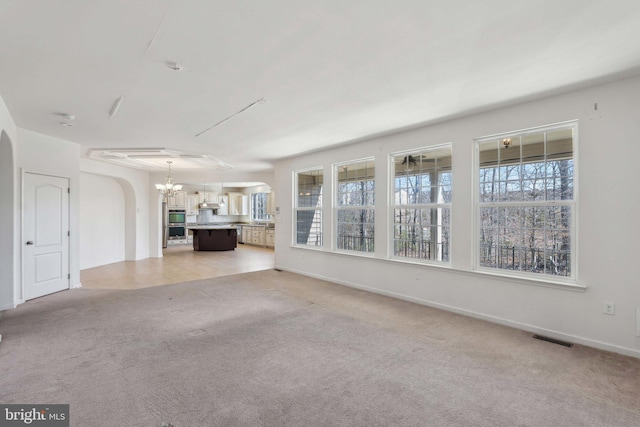 unfurnished living room featuring visible vents, baseboards, an inviting chandelier, arched walkways, and light colored carpet