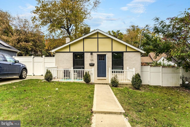 view of front of home featuring a front yard, fence, covered porch, a chimney, and brick siding