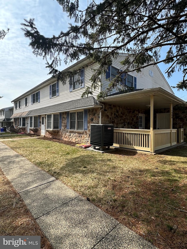 view of front of property featuring stone siding, cooling unit, and a front yard