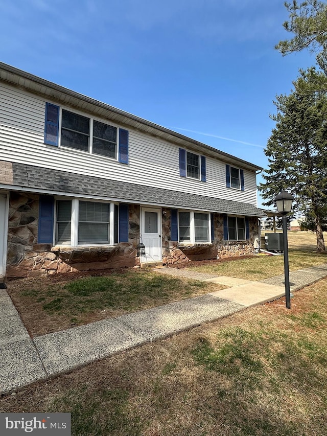 view of front of property featuring a front lawn, stone siding, and a shingled roof