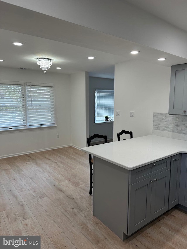 kitchen with decorative backsplash, gray cabinets, a peninsula, and light wood-type flooring