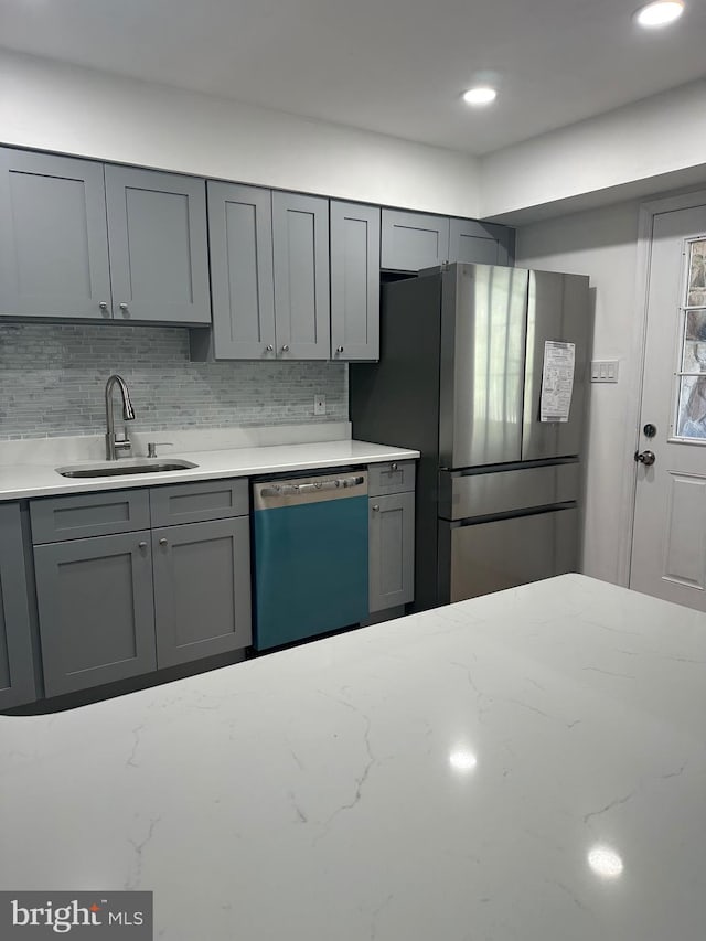 kitchen featuring dishwashing machine, gray cabinets, freestanding refrigerator, a sink, and decorative backsplash