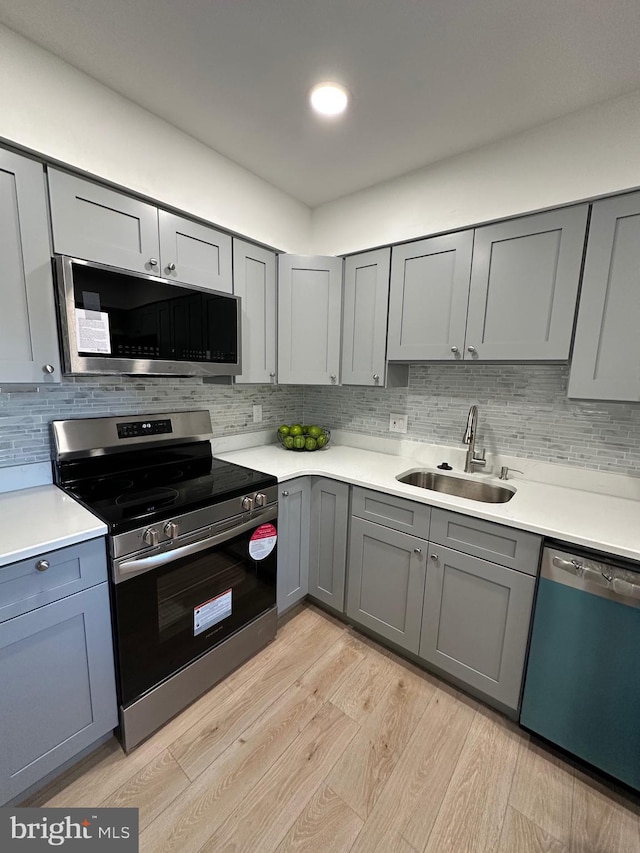 kitchen with gray cabinetry, a sink, tasteful backsplash, light wood-style floors, and appliances with stainless steel finishes