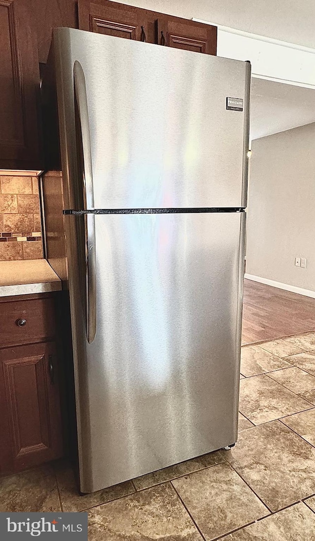 kitchen featuring dark brown cabinets, light countertops, freestanding refrigerator, and baseboards