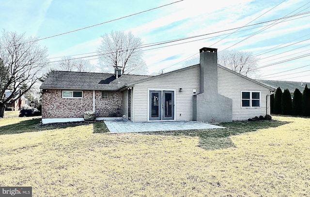 back of property with a yard, brick siding, a chimney, and a patio area