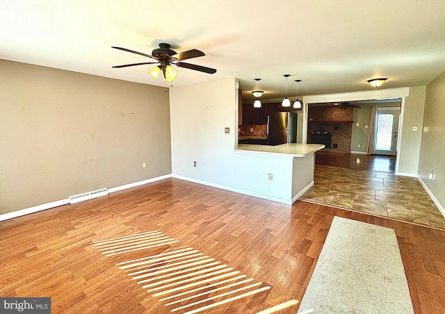 unfurnished living room with a ceiling fan, wood finished floors, visible vents, and baseboards