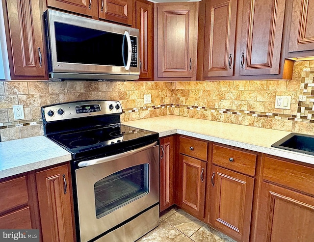 kitchen featuring stainless steel appliances, brown cabinetry, and light countertops