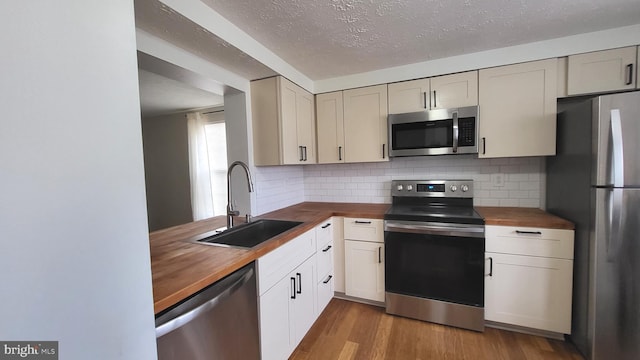 kitchen with a sink, stainless steel appliances, wood finished floors, and butcher block counters