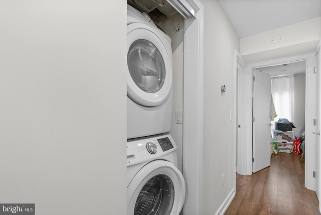 clothes washing area featuring laundry area, wood finished floors, and stacked washing maching and dryer