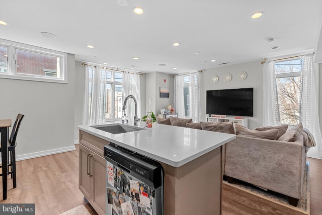 kitchen featuring light wood finished floors, open floor plan, light countertops, dishwashing machine, and a sink