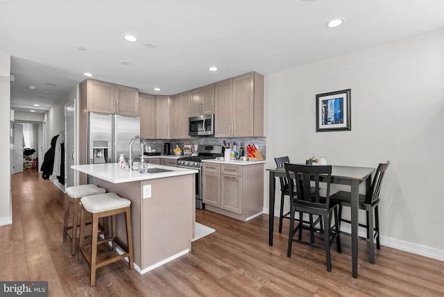 kitchen with wood finished floors, a sink, appliances with stainless steel finishes, a kitchen breakfast bar, and backsplash