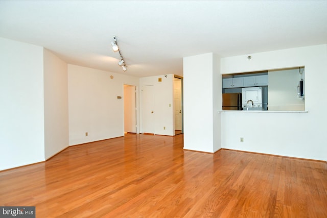 unfurnished living room with track lighting, light wood-type flooring, and a sink