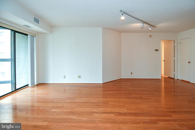 empty room with visible vents, light wood-style flooring, track lighting, and baseboards