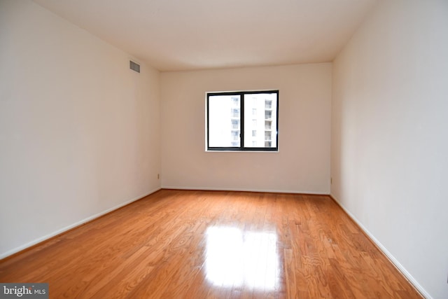 empty room featuring light wood-type flooring, visible vents, and baseboards