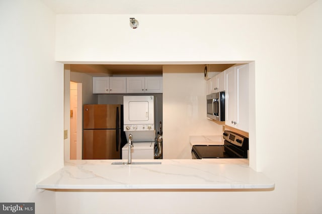 kitchen featuring light stone countertops, stacked washer and clothes dryer, appliances with stainless steel finishes, a peninsula, and a sink