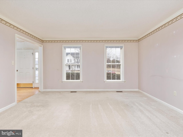 spare room featuring visible vents, light colored carpet, crown molding, and baseboards