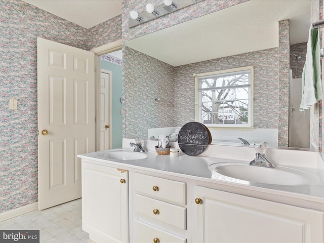 full bathroom with a sink, a textured ceiling, double vanity, and wallpapered walls