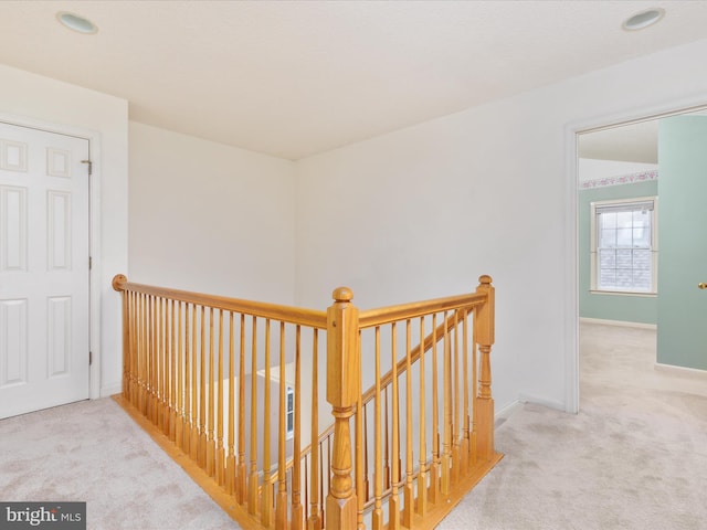 hallway with an upstairs landing, baseboards, and carpet floors