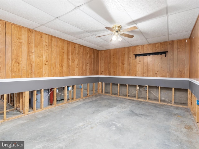 interior space with unfinished concrete flooring, wood walls, a paneled ceiling, and a ceiling fan