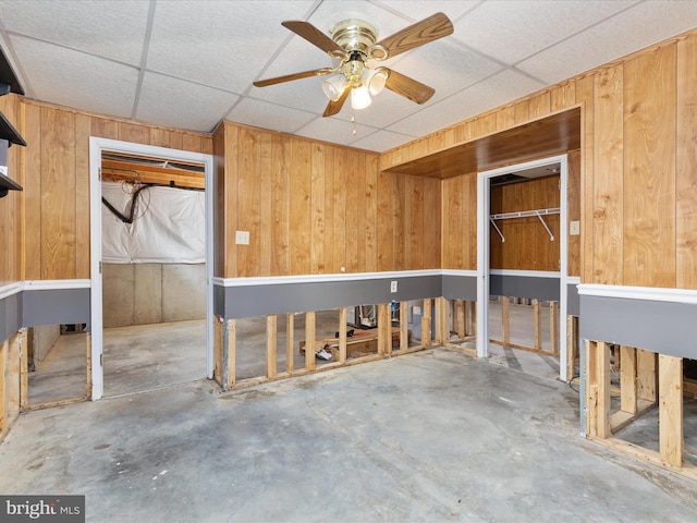 misc room with wooden walls, unfinished concrete floors, ceiling fan, and a drop ceiling