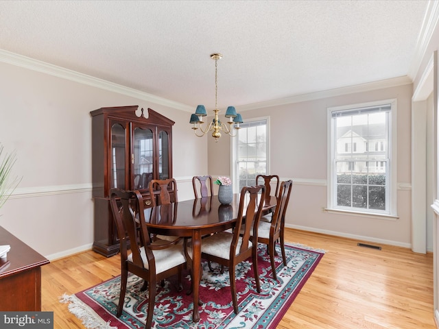 dining space with light wood-type flooring, a notable chandelier, ornamental molding, and a textured ceiling