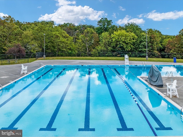 community pool featuring a patio area, fence, and a wooded view