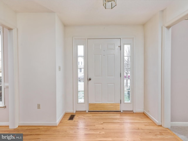 foyer entrance featuring visible vents, light wood-style flooring, and baseboards